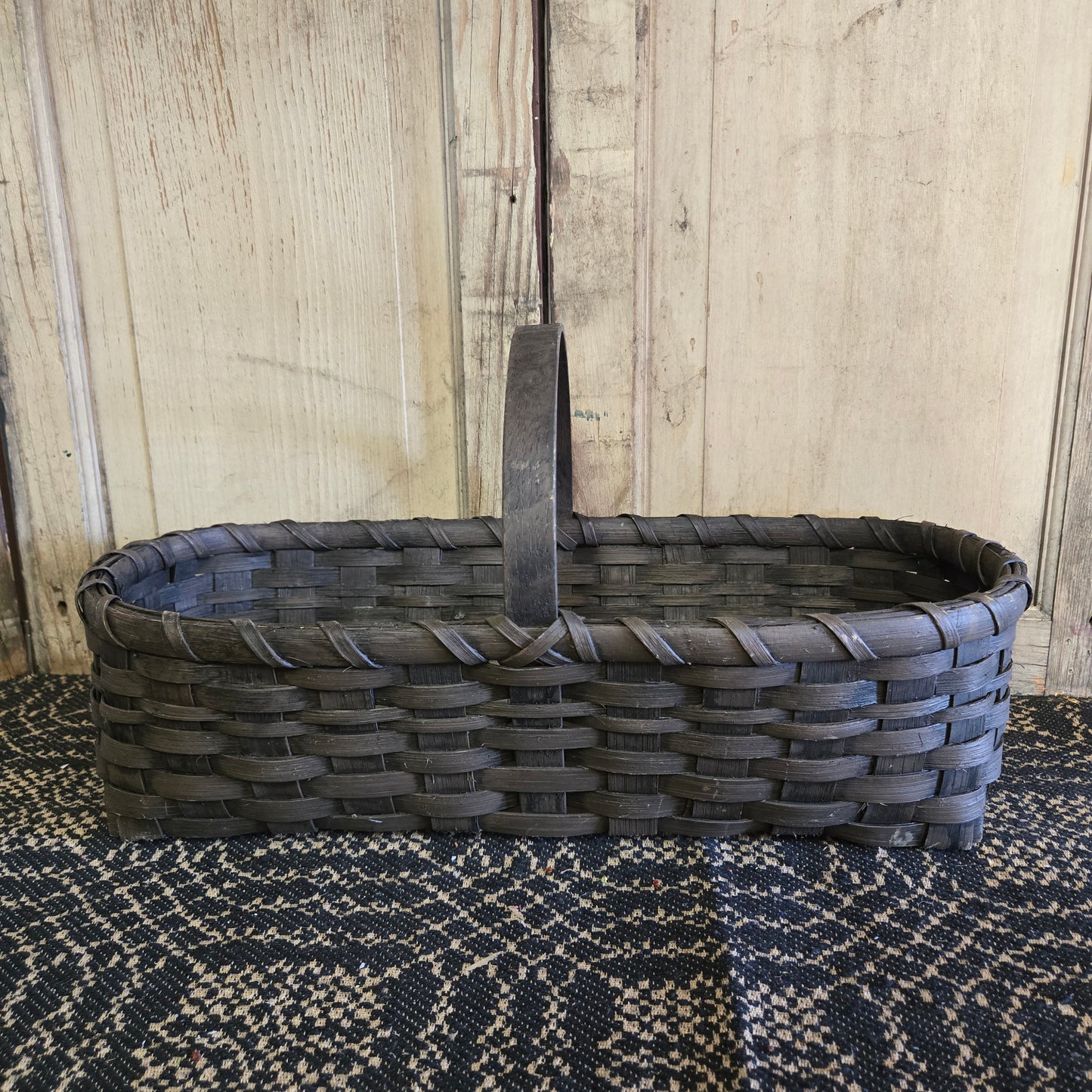 A handcrafted black rattan garden basket with a lid, placed on a textured surface against a wooden backdrop.