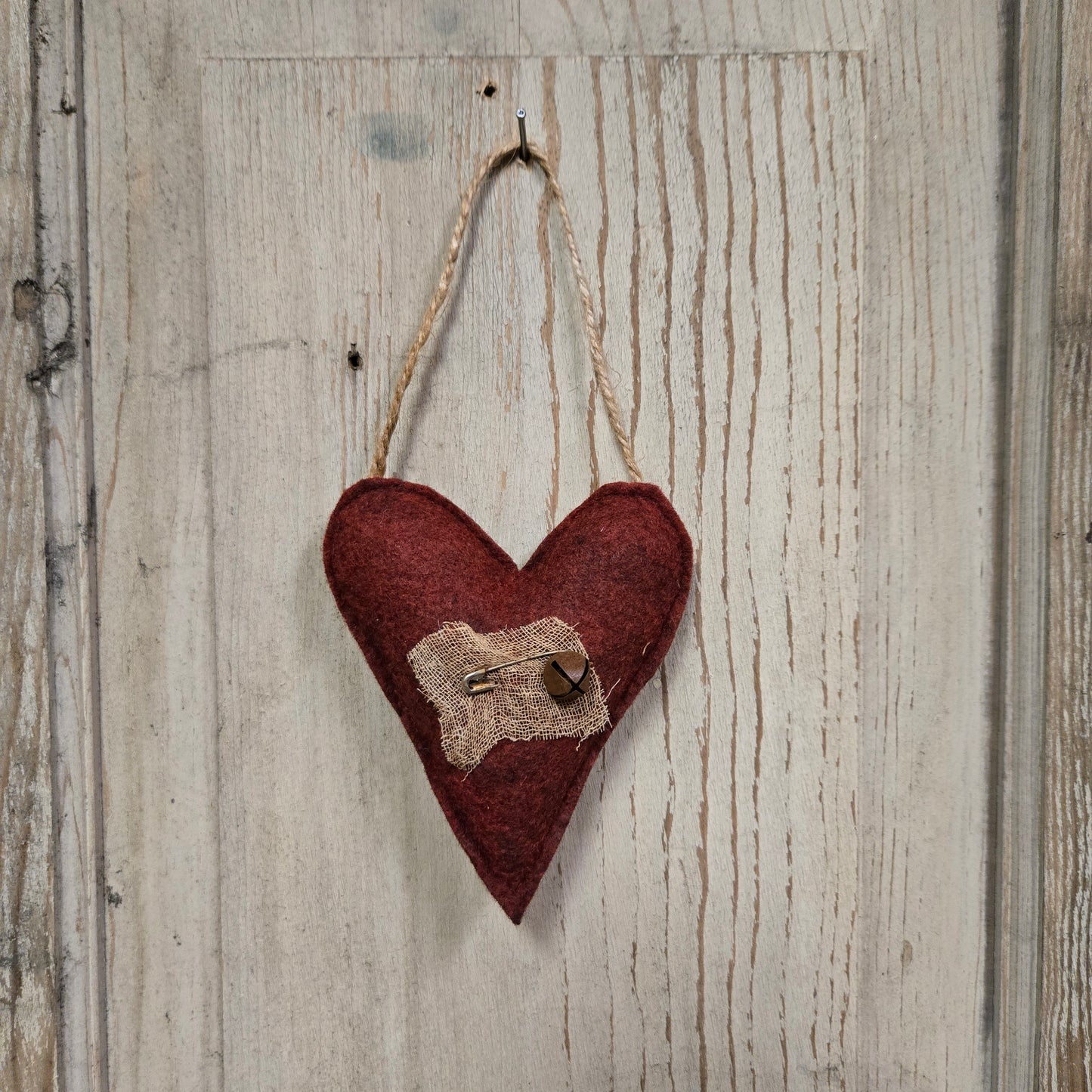 Red heart ornament suspended from a jute hanger hanging on a nail on a weathered board