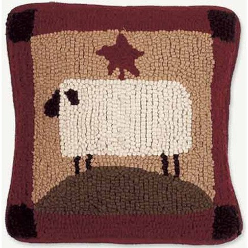 A square-shaped throw pillow with a hooked wool design featuring a sheep and part of a brown star-shaped pattern on a red background.