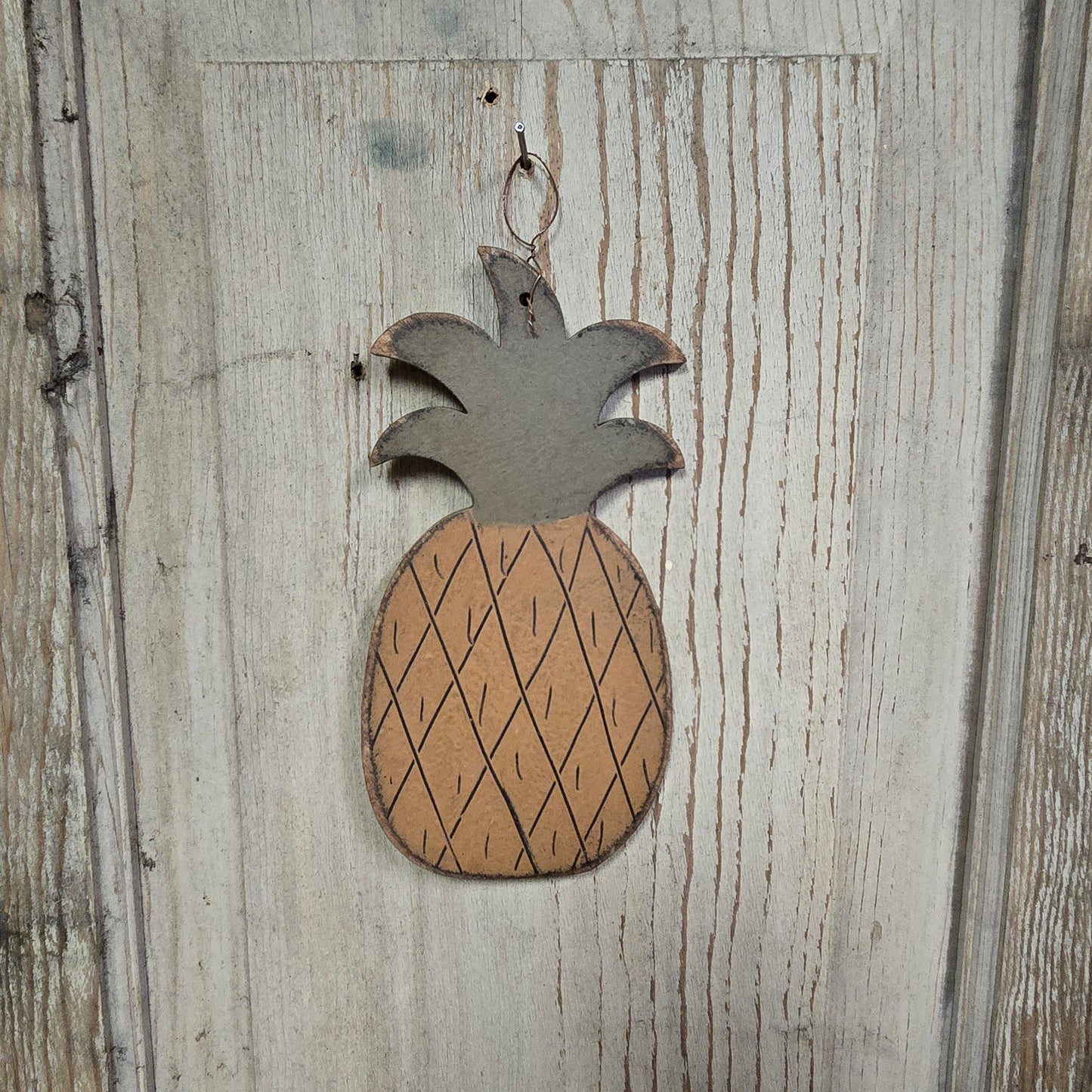 A wooden pineapple-shaped ornament hanging on a wooden door.