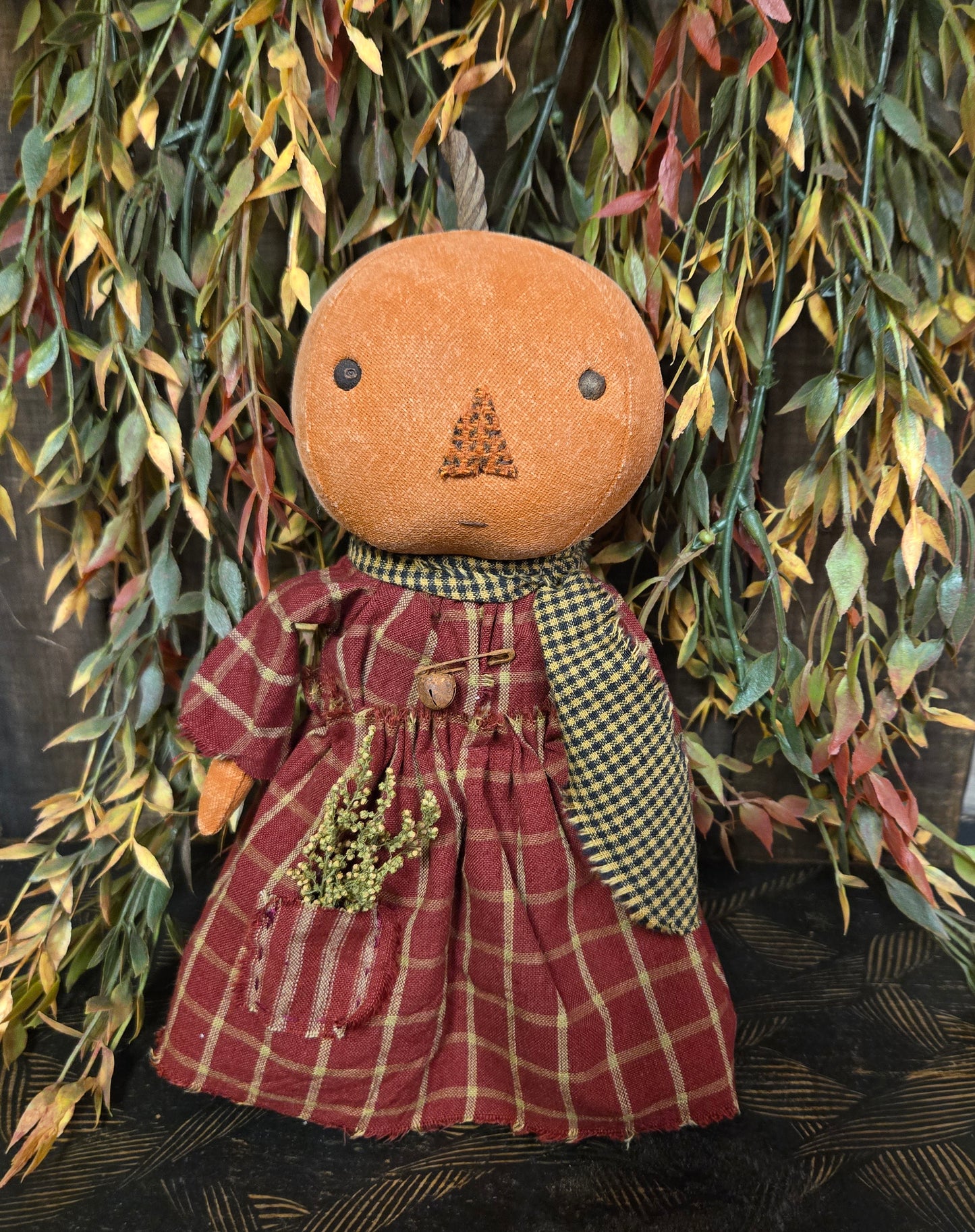 Vintage-style doll with plaid dress and checkered apron against a leafy background
