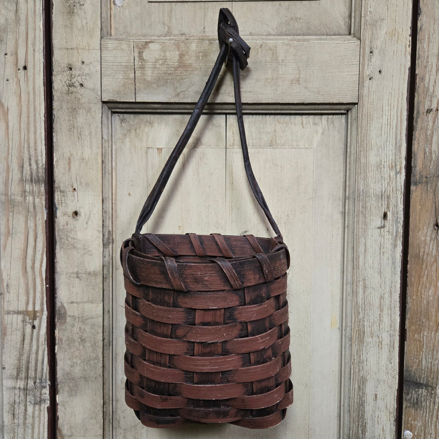 A burgundy basket hanging on a door knob.