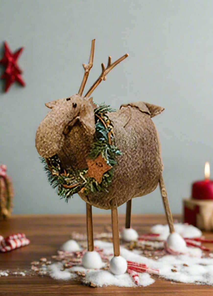 Primitive reindeer ornament with wreath around neck on white bench