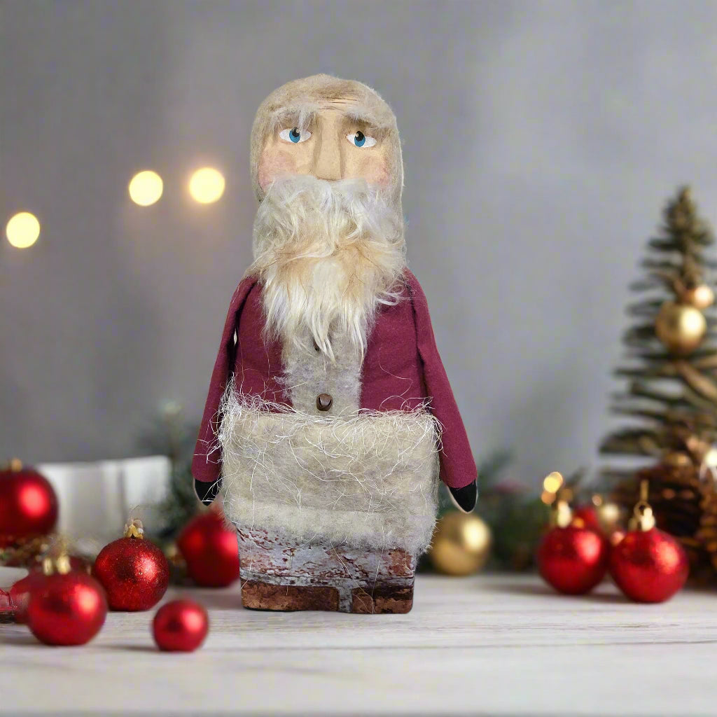 Handmade Santa Claus figurine with Christmas decorations on a wooden table.