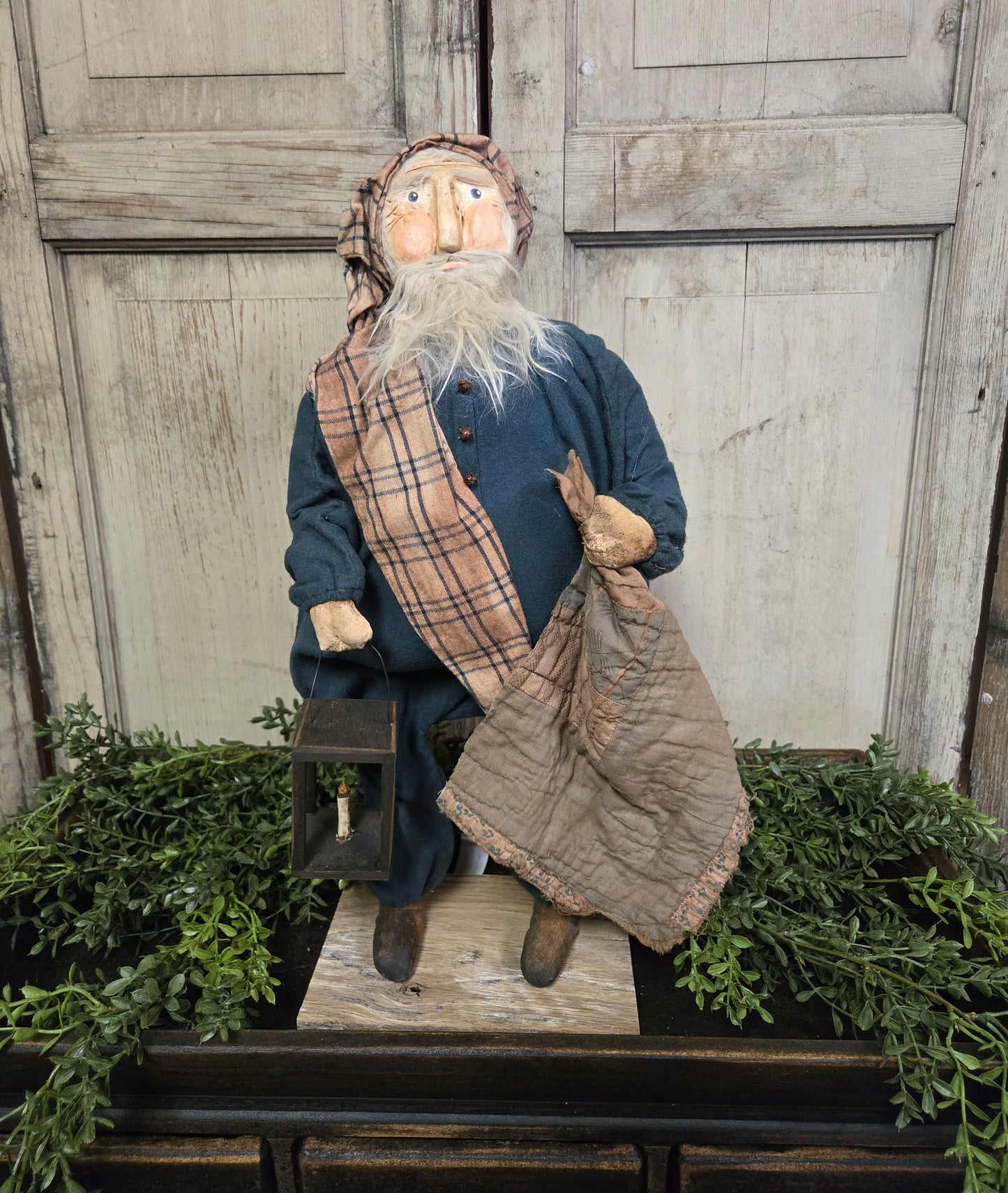 Primitive Santa with Lantern, featuring a traditional lantern and a clay face with a plaid scarf, standing on a platform with holiday decor.