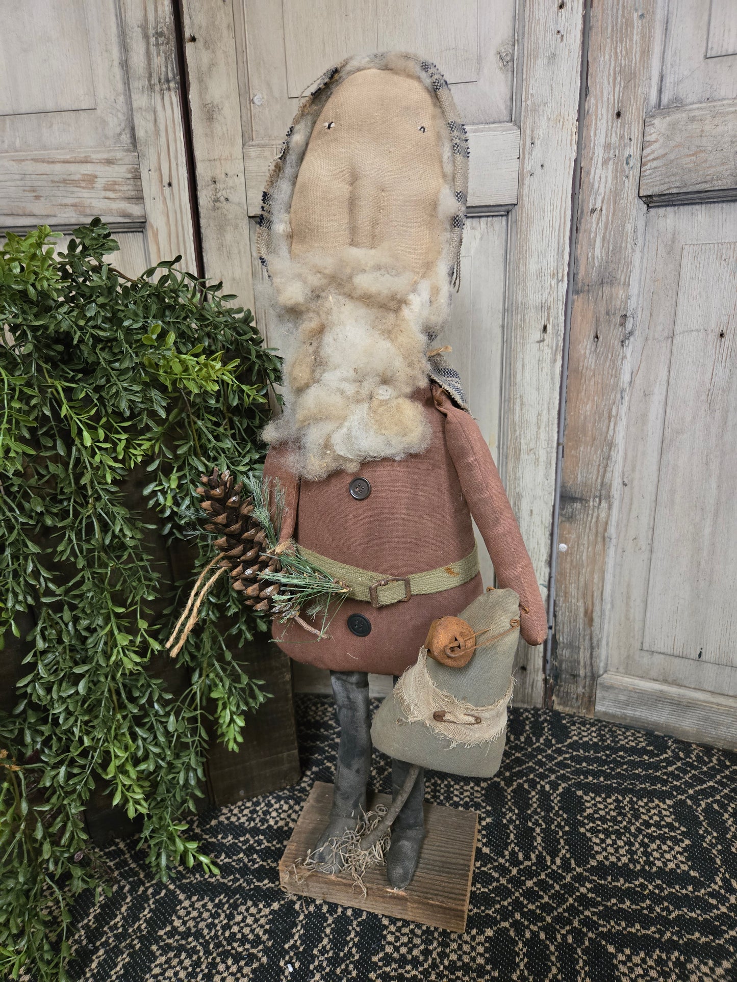 Decorative Santa with a beard and hat, standing on a wooden floor with greenery.
