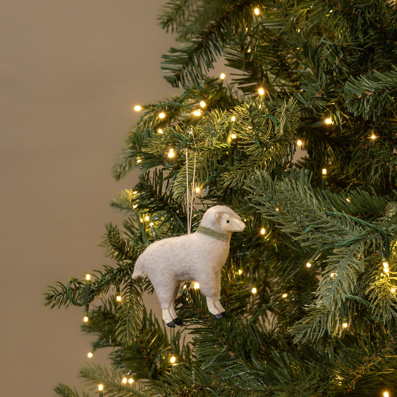 White sheep ornament on a decorated Christmas tree with lights.