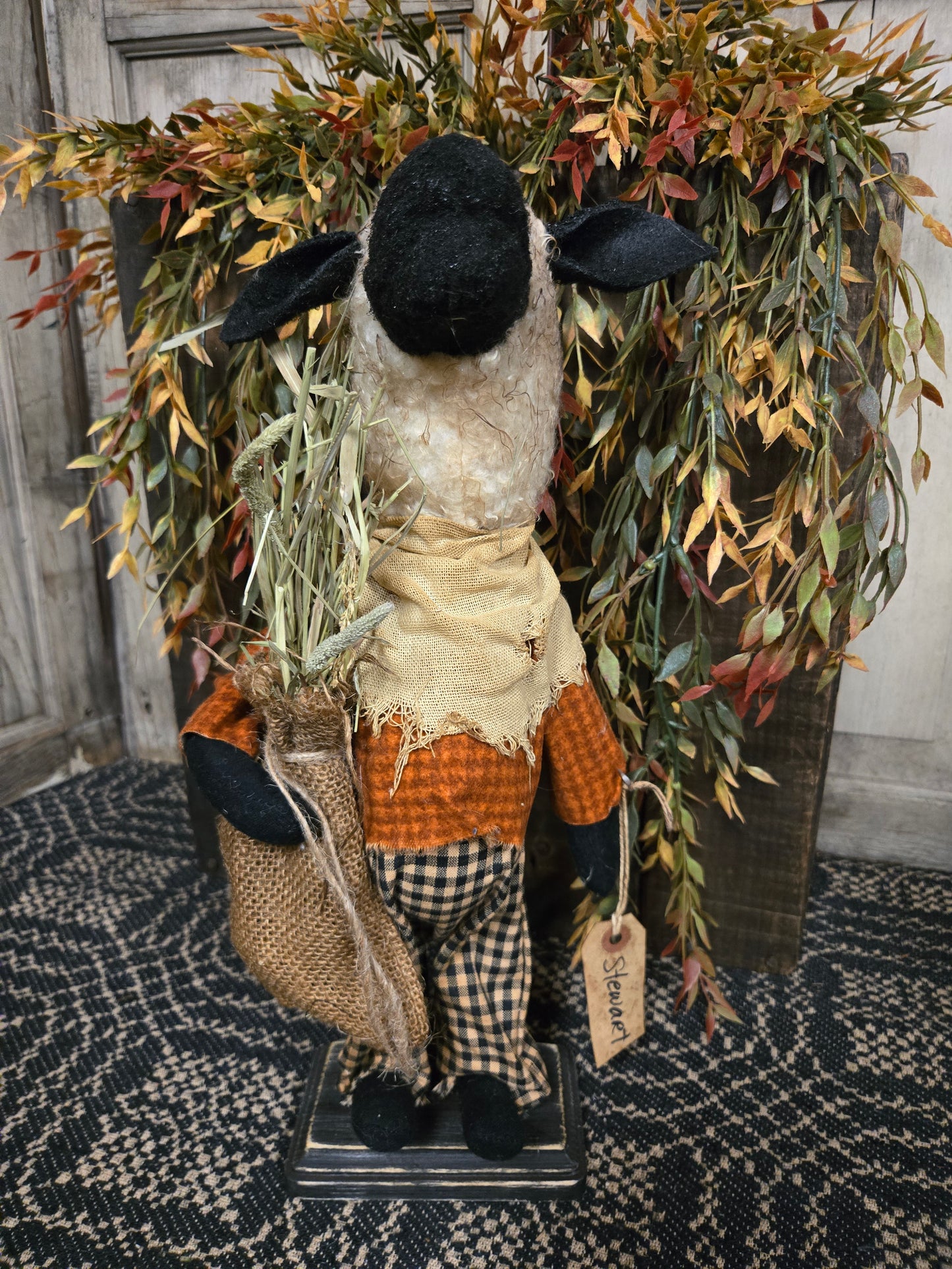 Decorative sheep figure with plaid outfit and black boots on a textured surface with foliage.
