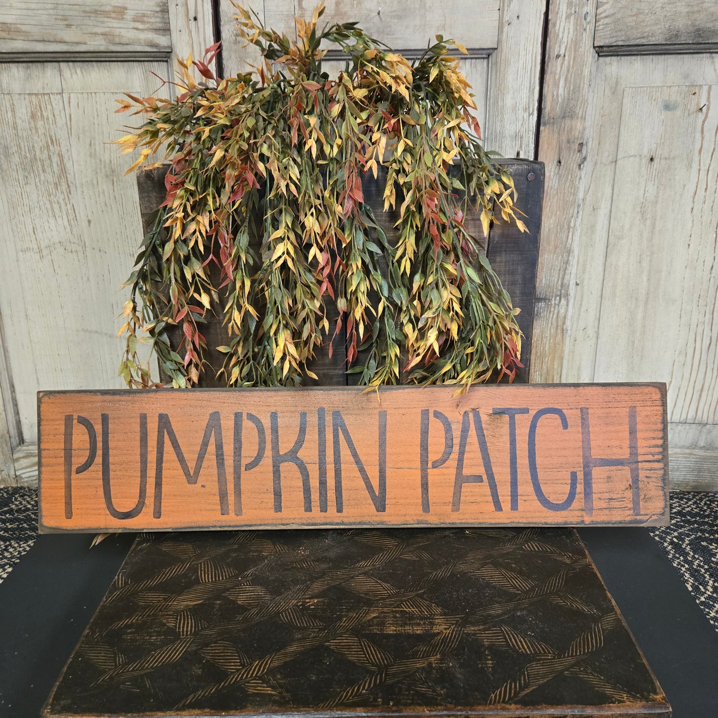 Wooden sign with 'Pumpkin Patch' text next to a wreath on a door.