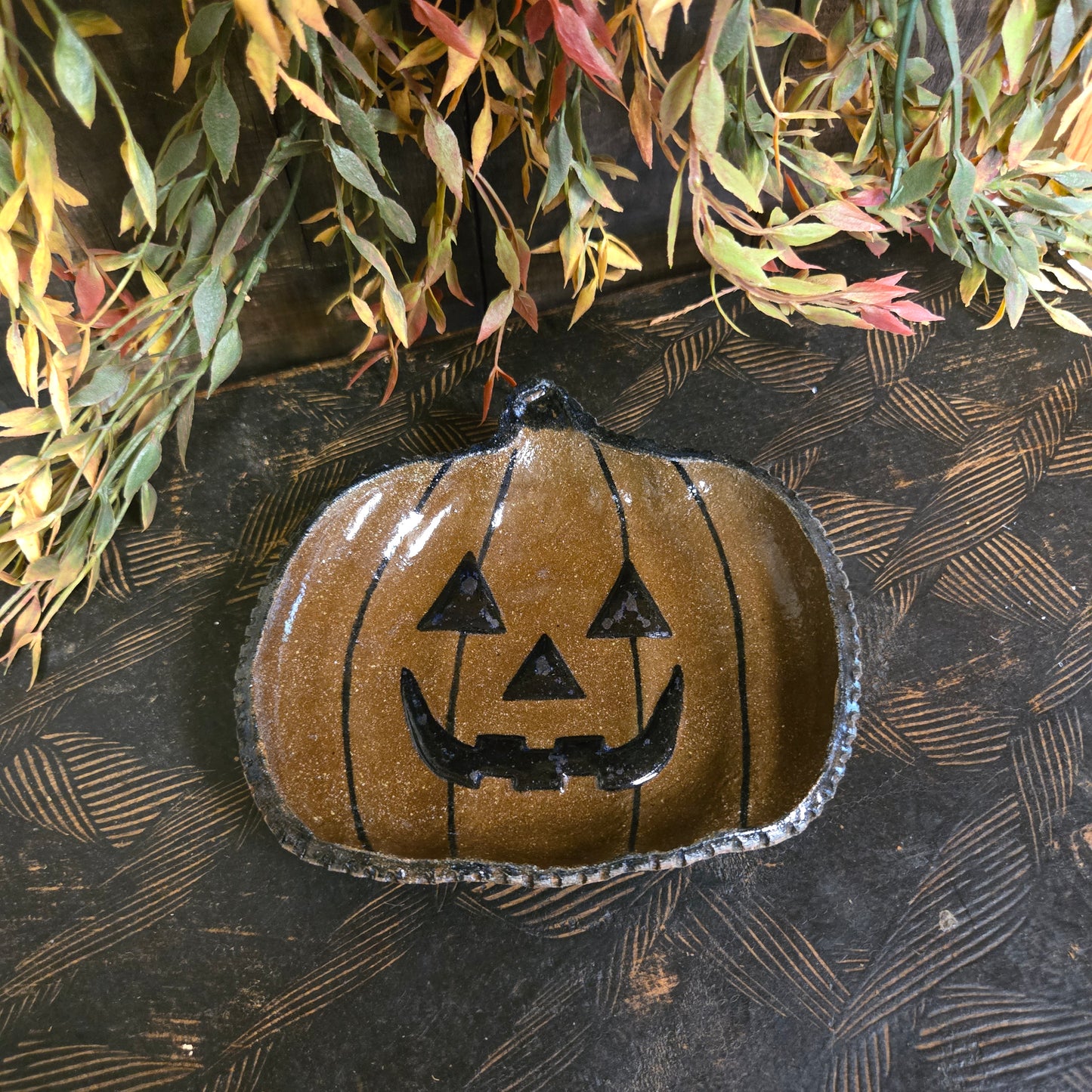 Decorative pumpkin shape plate with face design on a textured surface with leaves.