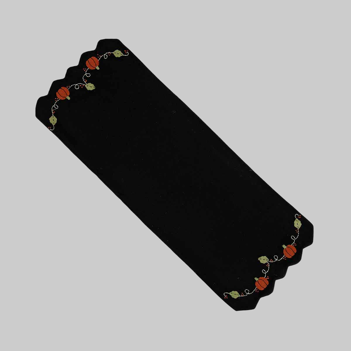 A black wool felt table runner with a floral pattern that includes pumpkins and vines, bordered by a decorative braided edge.