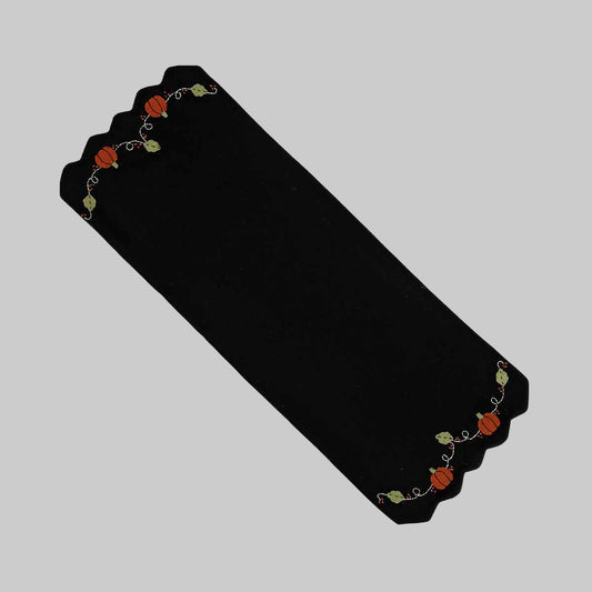 A black wool felt table runner with a floral pattern that includes pumpkins and vines, bordered by a decorative braided edge.