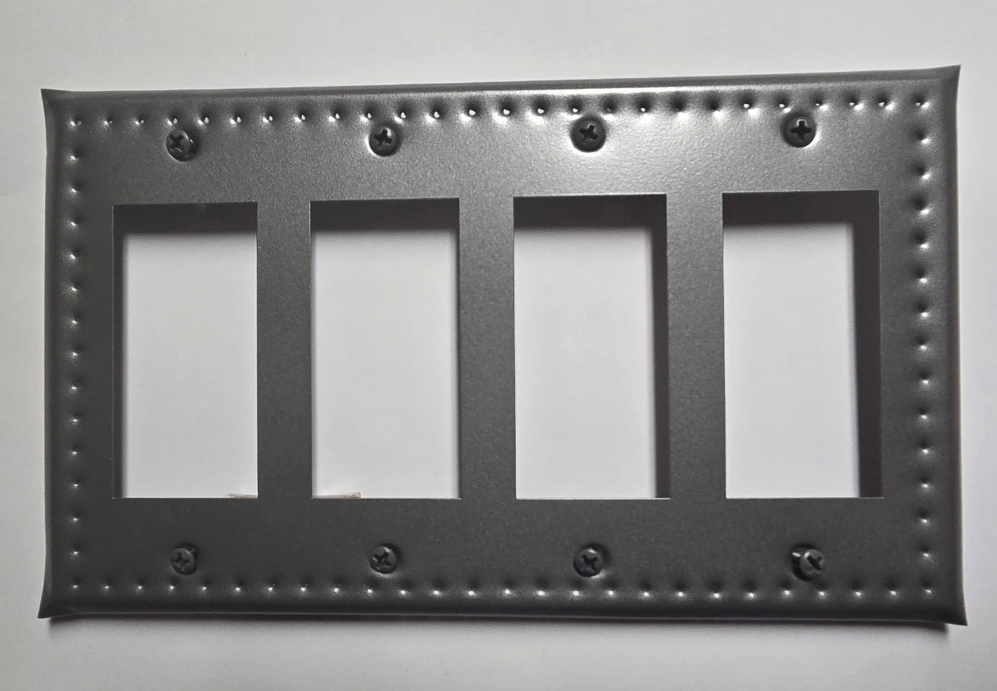 Decorative black metal switch plate with four blank panels on a white background