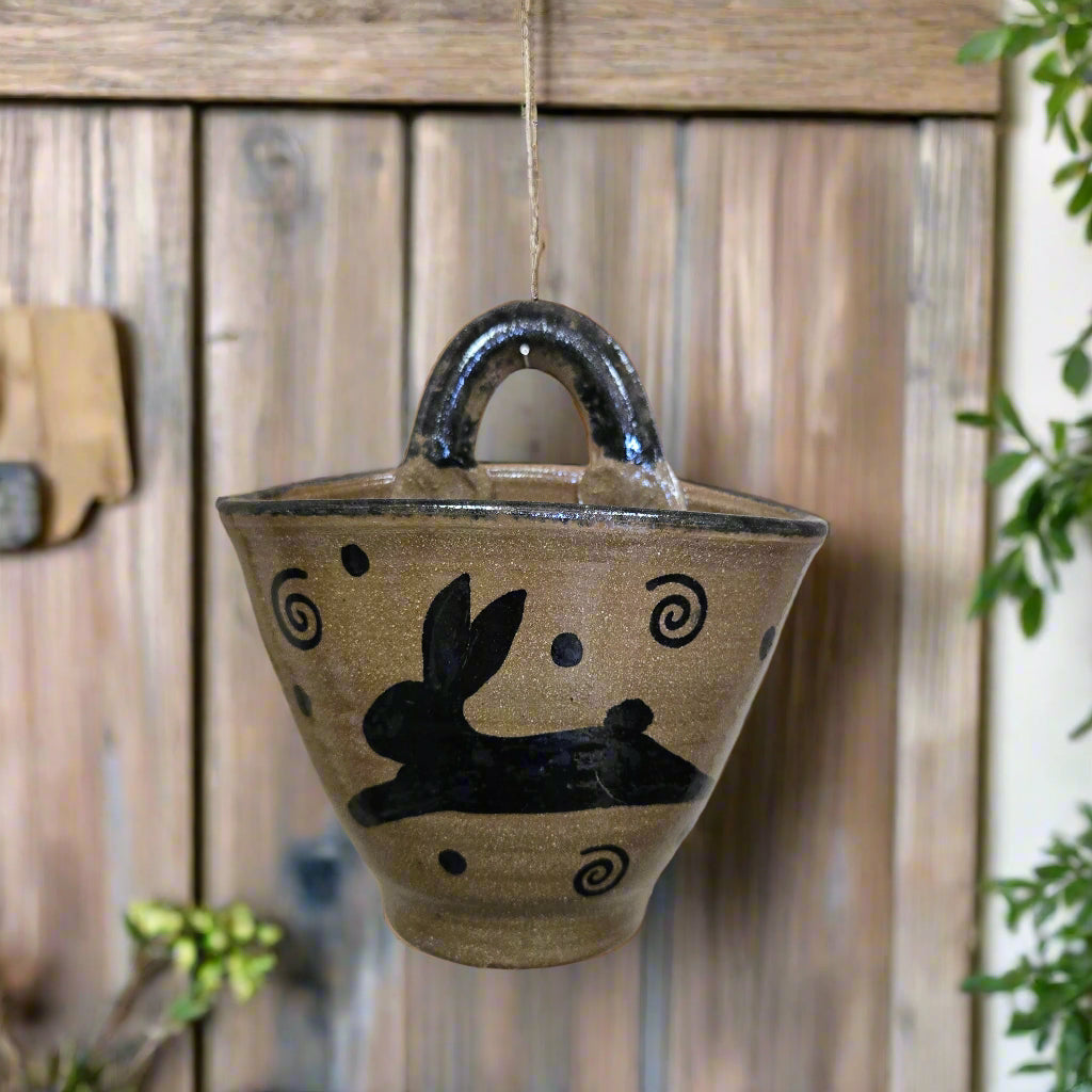 A handcrafted stoneware wall pocket with a brown base color and black rabbit pattern, mounted on a wooden surface.