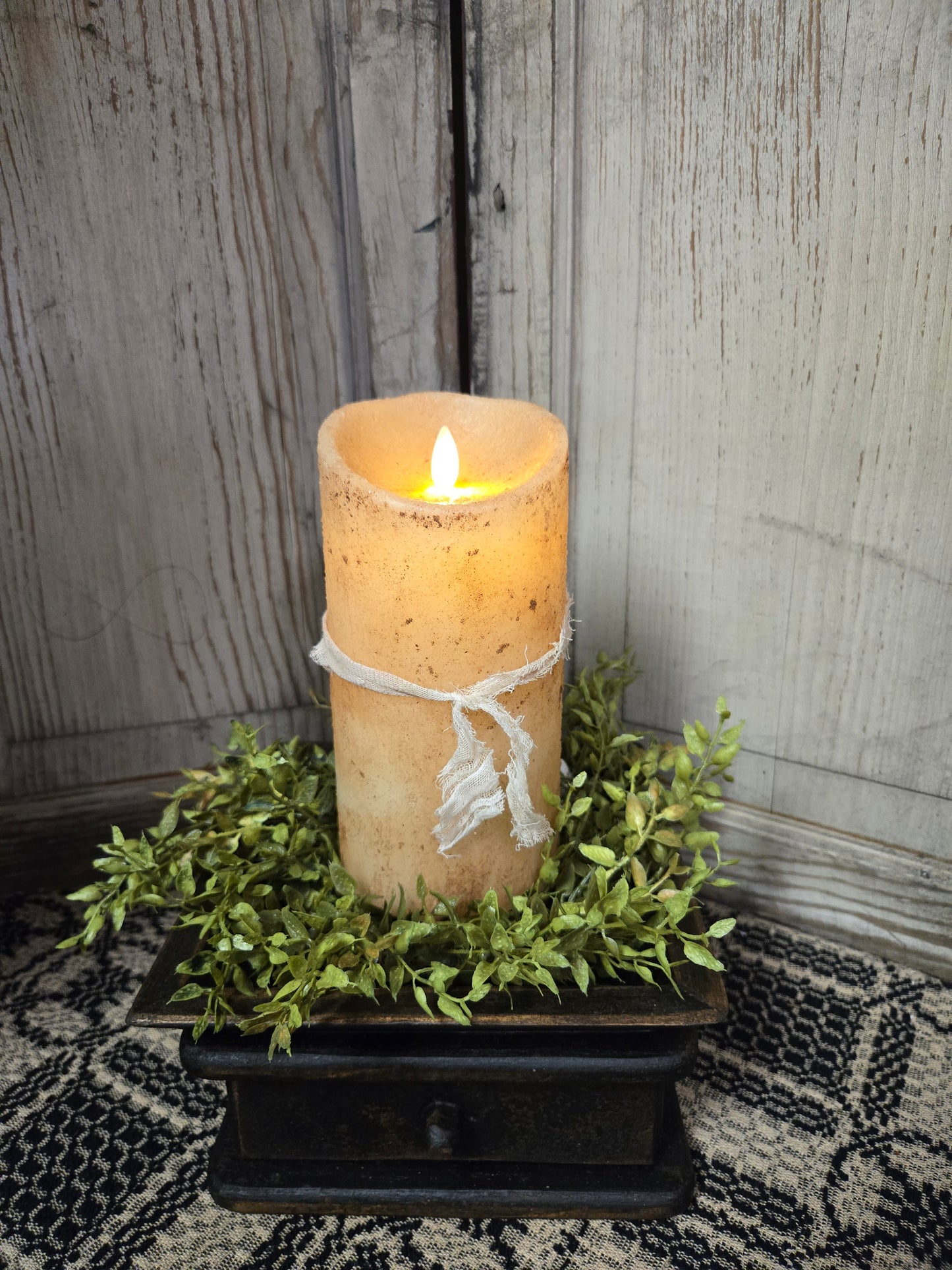 A 7-inch tall burnt ivory pillar candle with a moving flame effect, placed on a decorative tray with greenery around it.