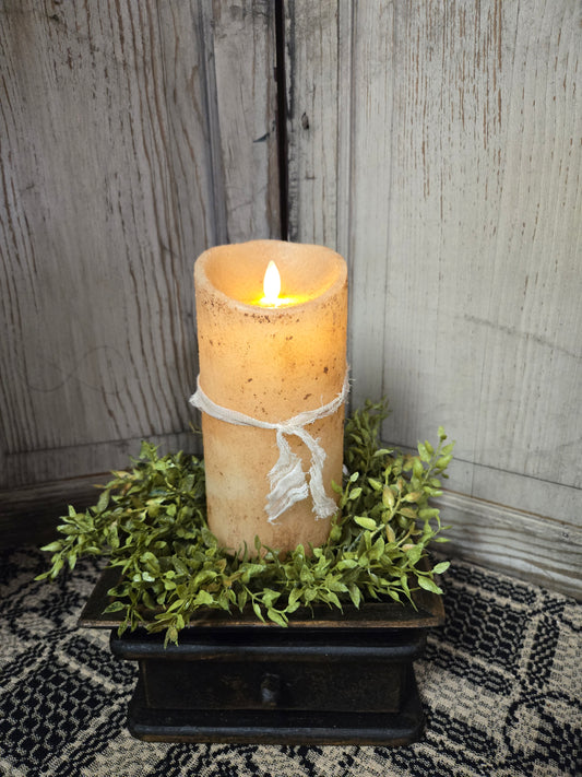 A 7-inch tall burnt ivory pillar candle with a moving flame effect, placed on a decorative tray with greenery around it.