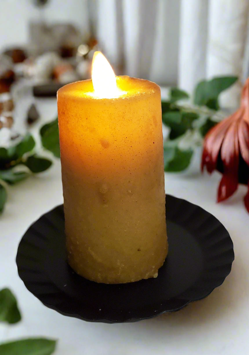 A realistic moving flame mini pillar candle burnt ivory in color, placed on a black dish.