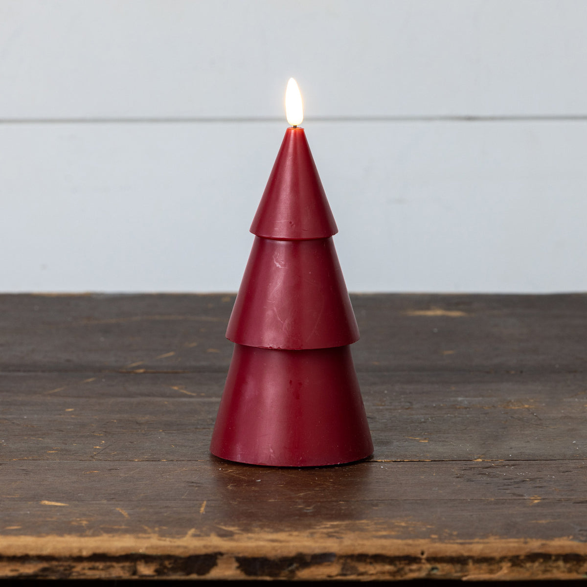 Red candle shaped like a Christmas tree on a wooden surface with a light gray background