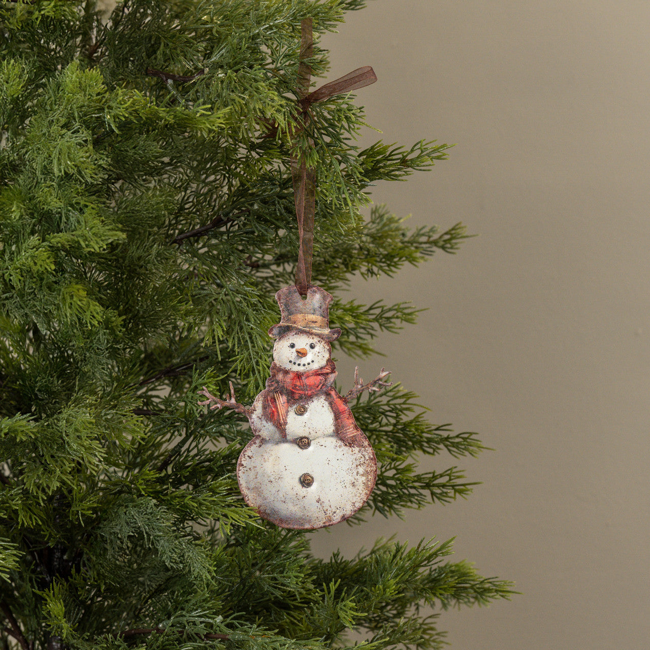 Decorative snowman ornament hanging on a Christmas tree branch.