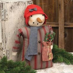 A primitive snowman doll with a red cap and a sack of Christmas greenery. The doll is dressed in a vintage-style coat with red and black stripes and a grey scarf.