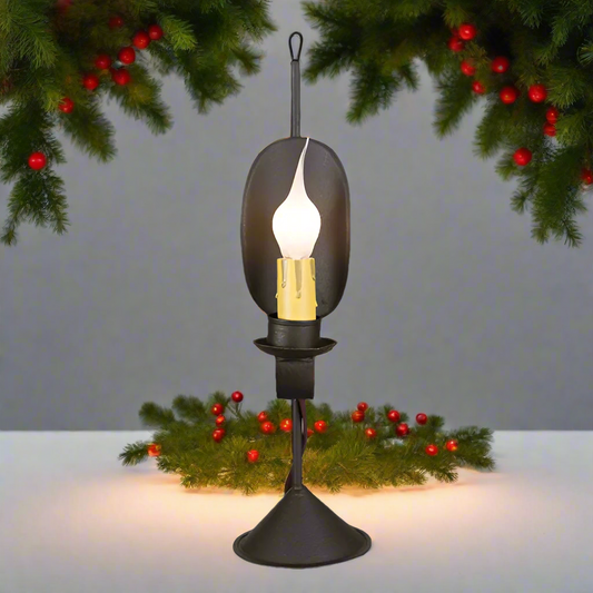 A black table lamp shown on a white table with Christmas greenery in the background.