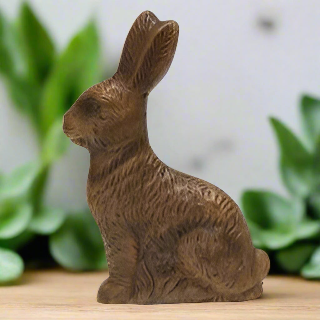 A brown, resin figurine of a chocolate bunny with carved details, standing on a flat surface.