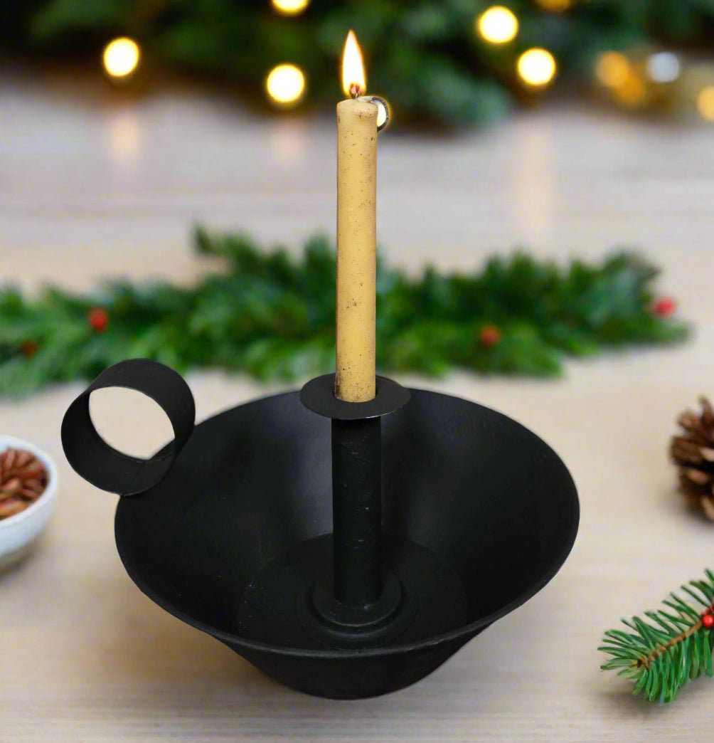 Black candle holder with a lit candle on a wooden surface with Christmas decorations.