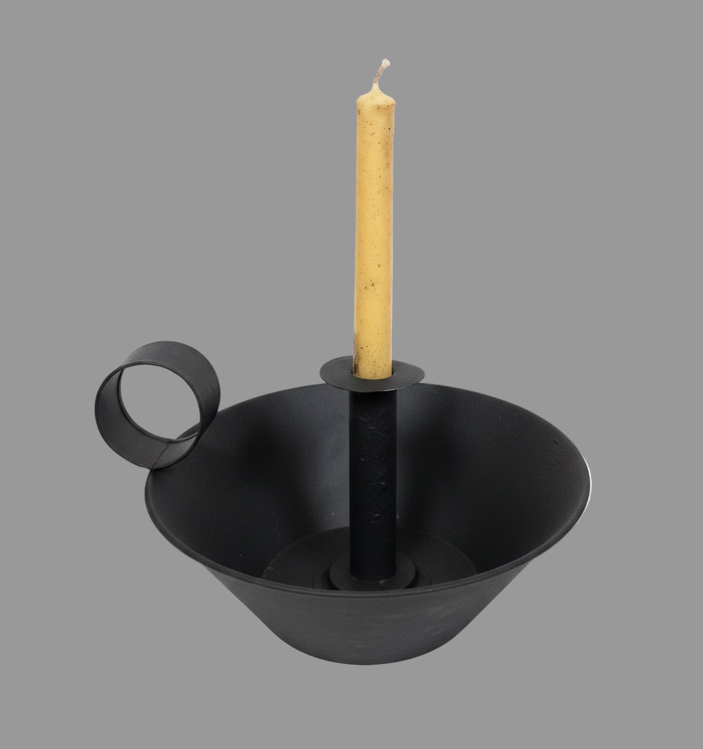 Black candle holder with a lit candle on a wooden surface with Christmas decorations.