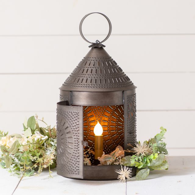 Primitive tin revere accent light with one bulb and greenery in background.