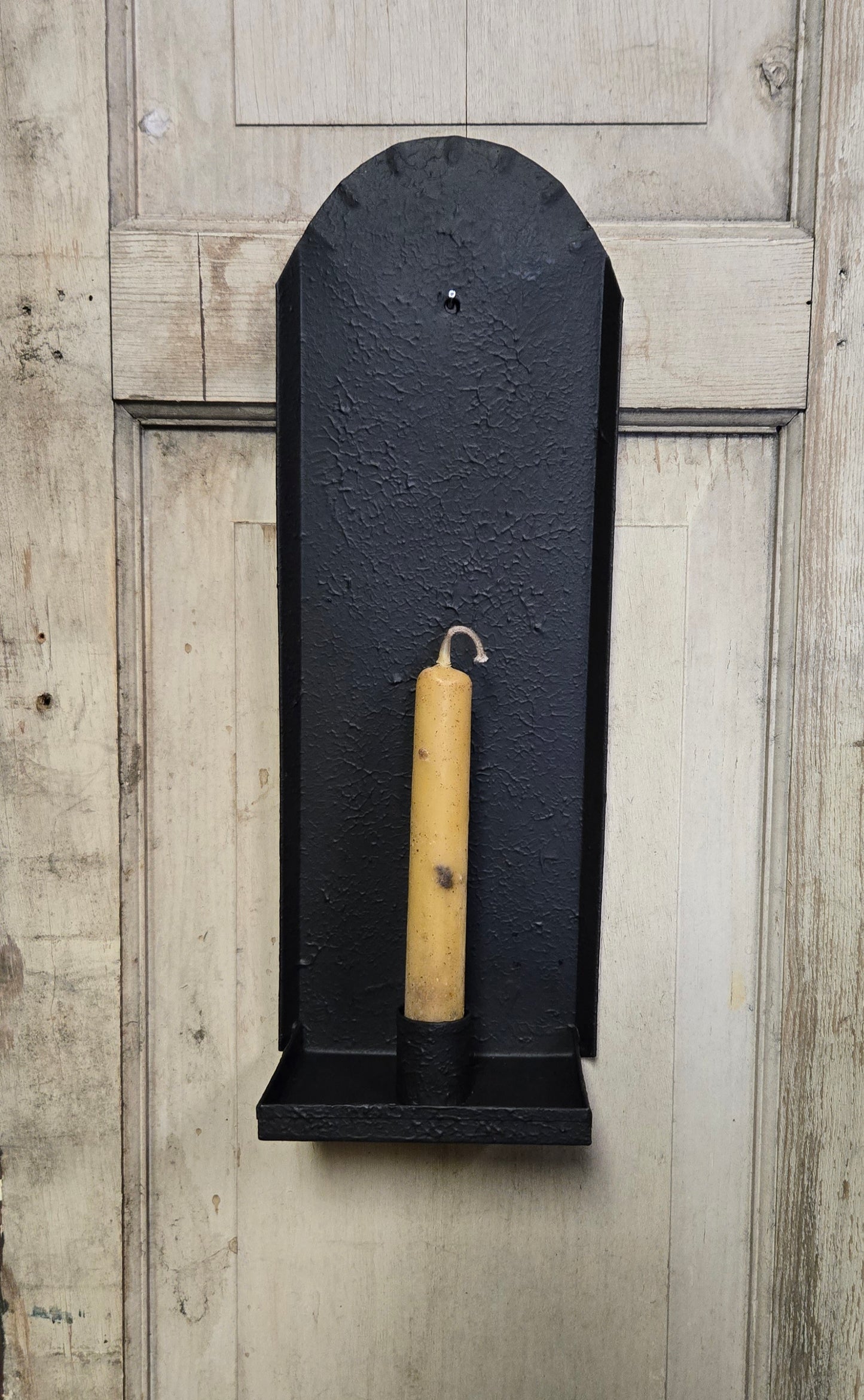 Black wall-mounted sconce with one candle on a wooden background