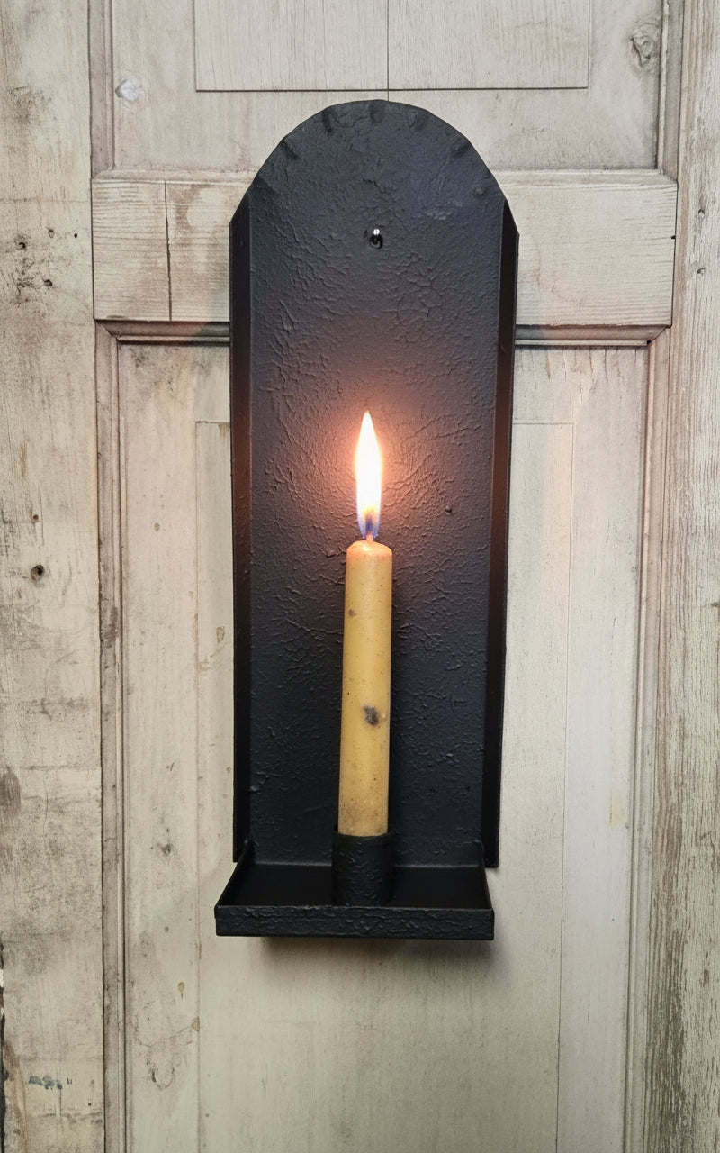 Black wall-mounted sconce with one candle on a wooden background