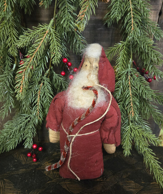 Textile figurine of a bearded man in a red coat with white trim, surrounded by greenery and berries.