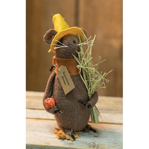 Stuffed mouse toy with a yellow hat, brown outfit, and holding hay and a pumpkin on a wooden surface.