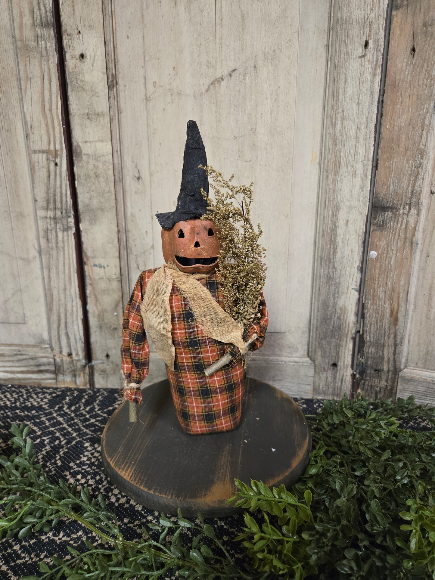 Pumpkin head doll with witch hat holding a sprig of Sweet Annie