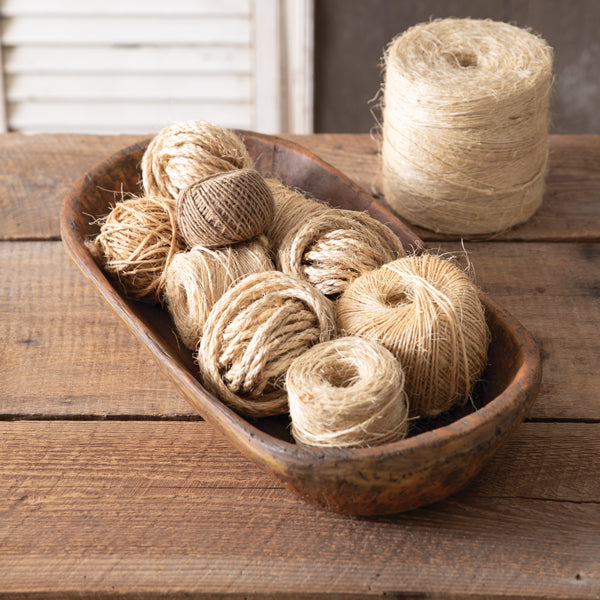 A brown, resin shallow tub filled with brown yarn and a few knitted items, placed on a wooden surface.