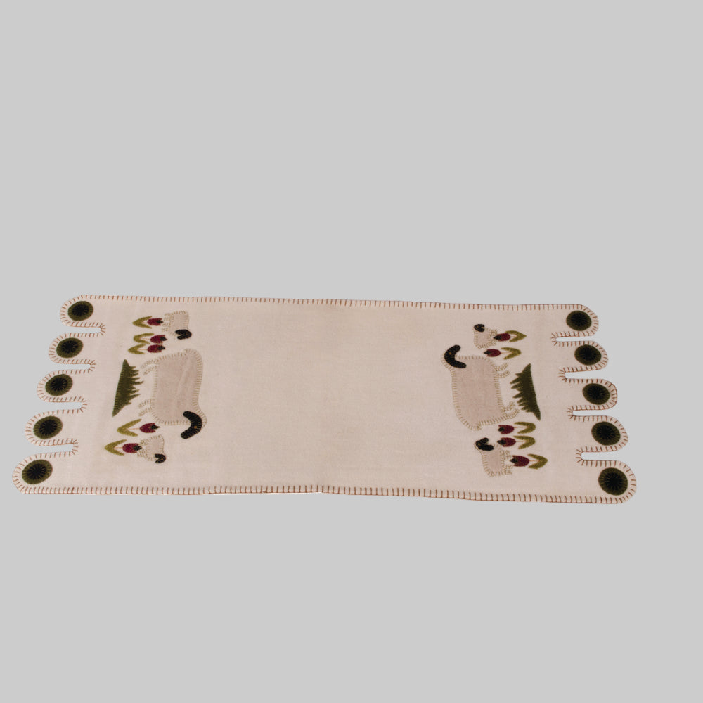 A beige table runner with an embroidered design of sheep in a meadow, featuring a repeated pattern of sheep and greenery.