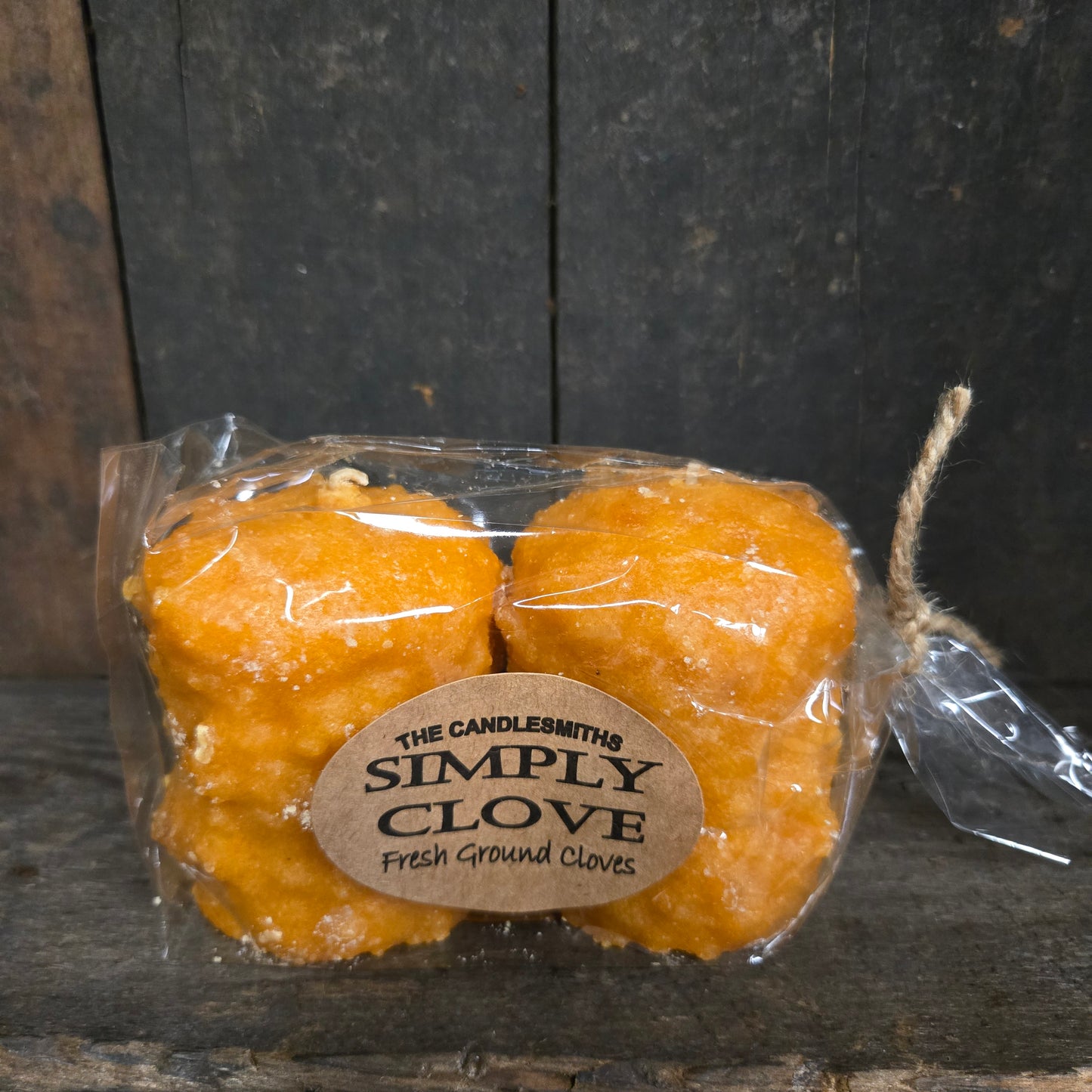 Two wrapped candles with a 'Simply Clove' label on a dark wooden surface