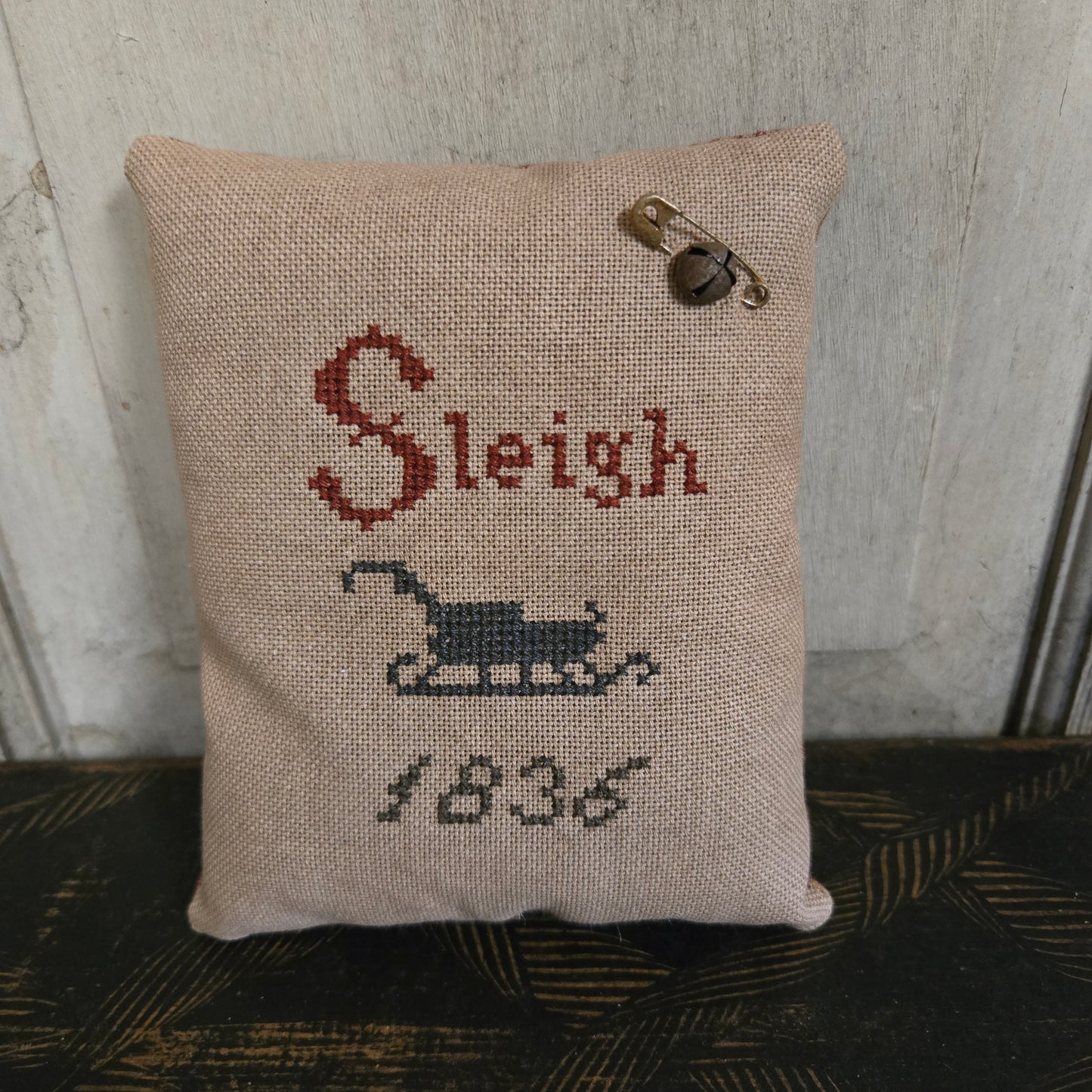 Decorative pillow with cross-stitched text and design on a textured surface