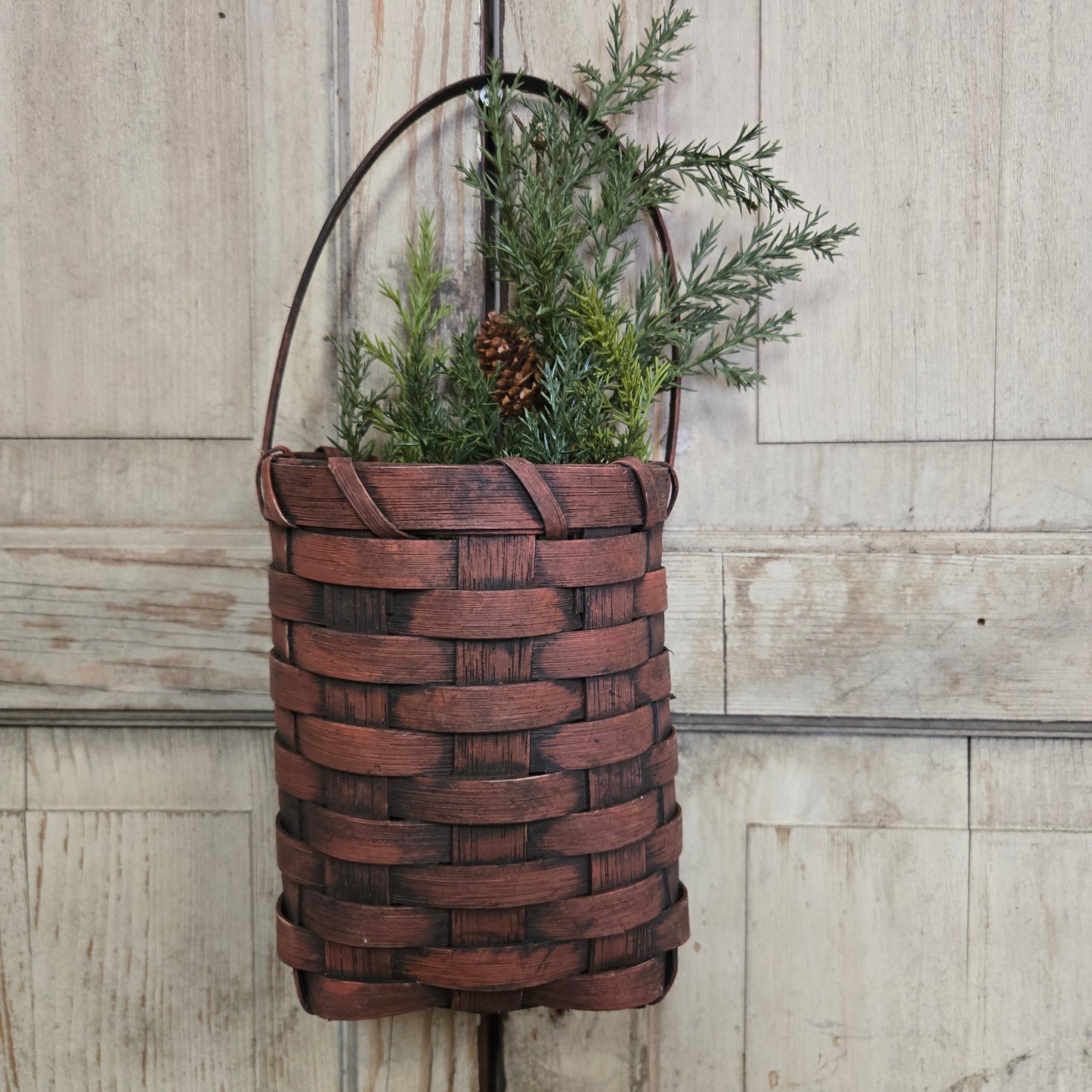 Woven brown basket with greenery on a wooden surface