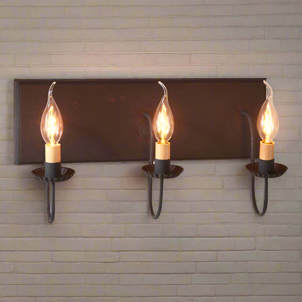 A three-light vanity light fixture with a black backplate and red textured arms, featuring E12/Candelabra sockets.