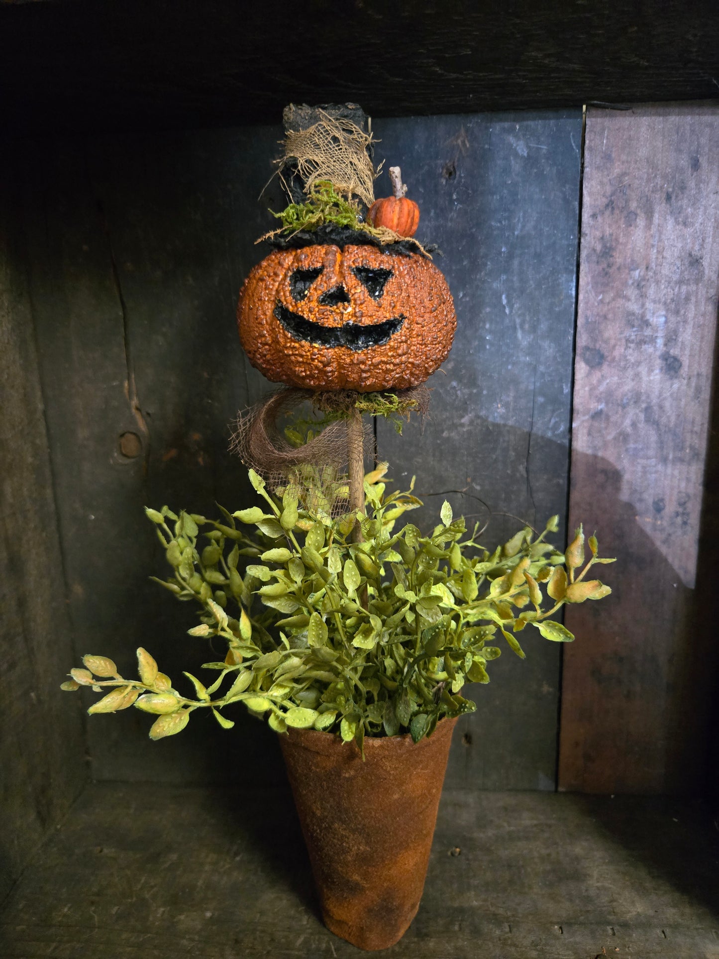 Decorative item with a carved pumpkin and greenery on a rustic wooden surface