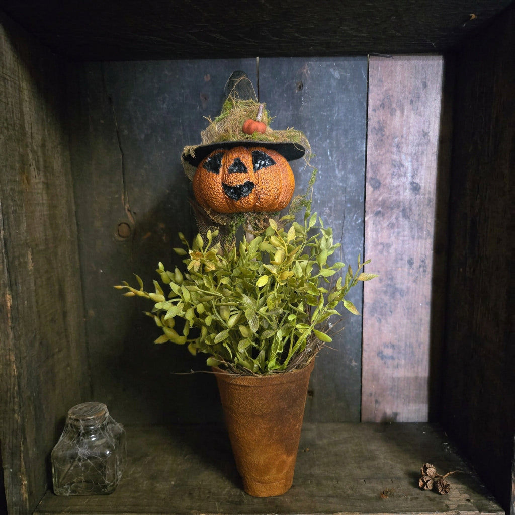 Potted plant with a Halloween-themed pumpkin topiary against a rustic wooden background