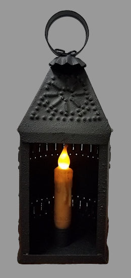 A black textured metal candle lantern with a candle lit inside, designed for use with a 4-inch taper candle (not included).
