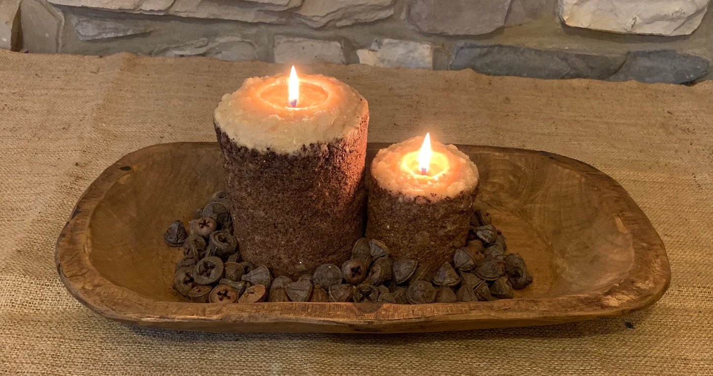 Two lit candles on a wooden tray with stones on a stone surface