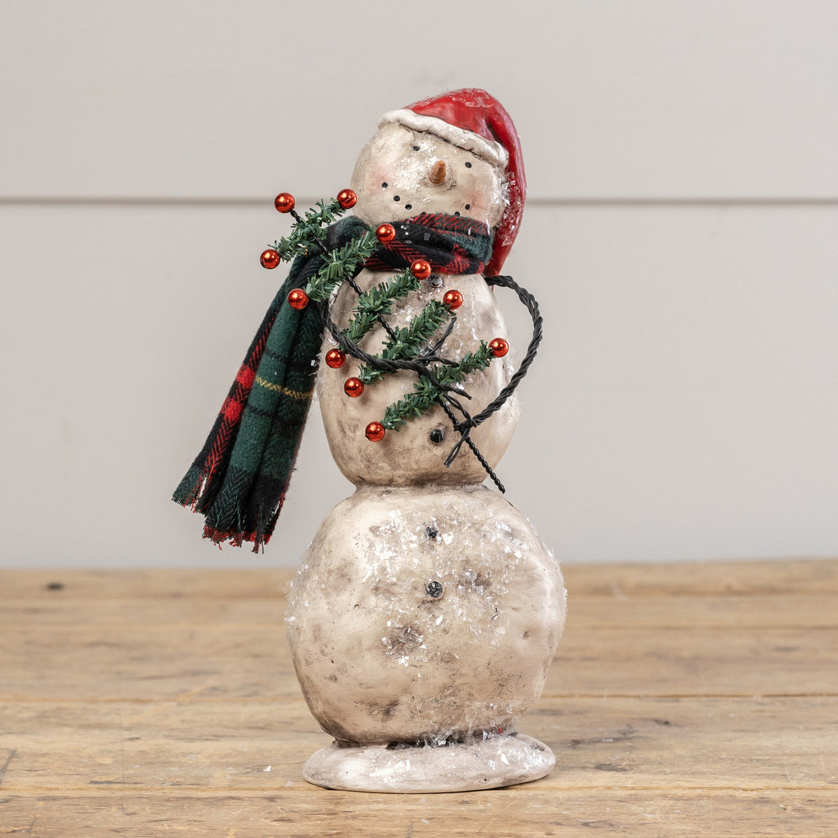 Decorative snowman figurine with a red hat and green scarf on a wooden surface.