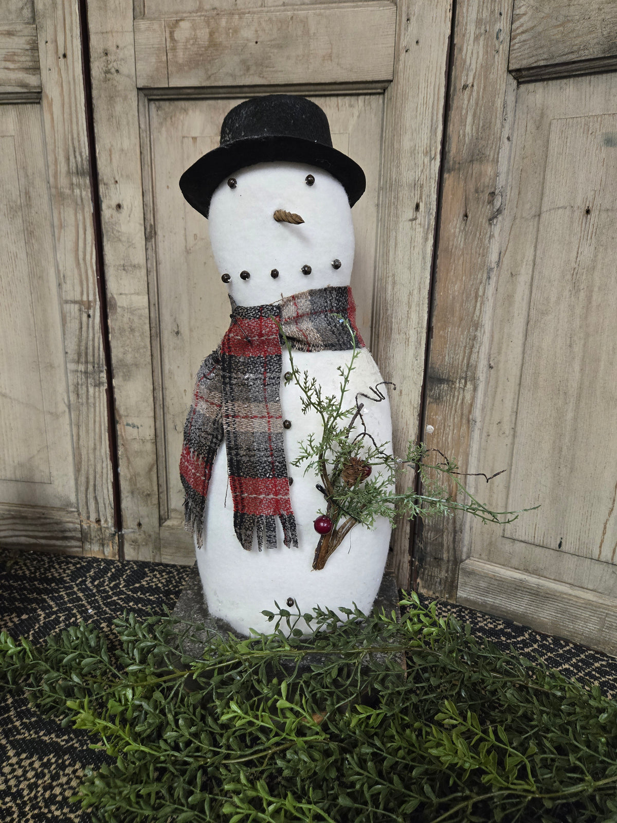 Decorative snowman with a top hat, scarf, and branches against a wooden background