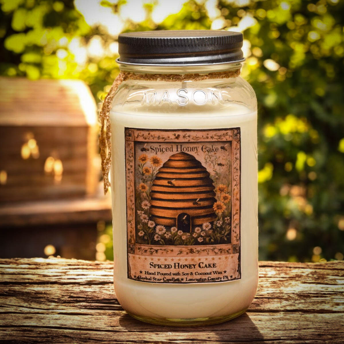 Jar candle labeled 'Spiced Honey Cake' with a bee hive design on a wooden surface outdoors.