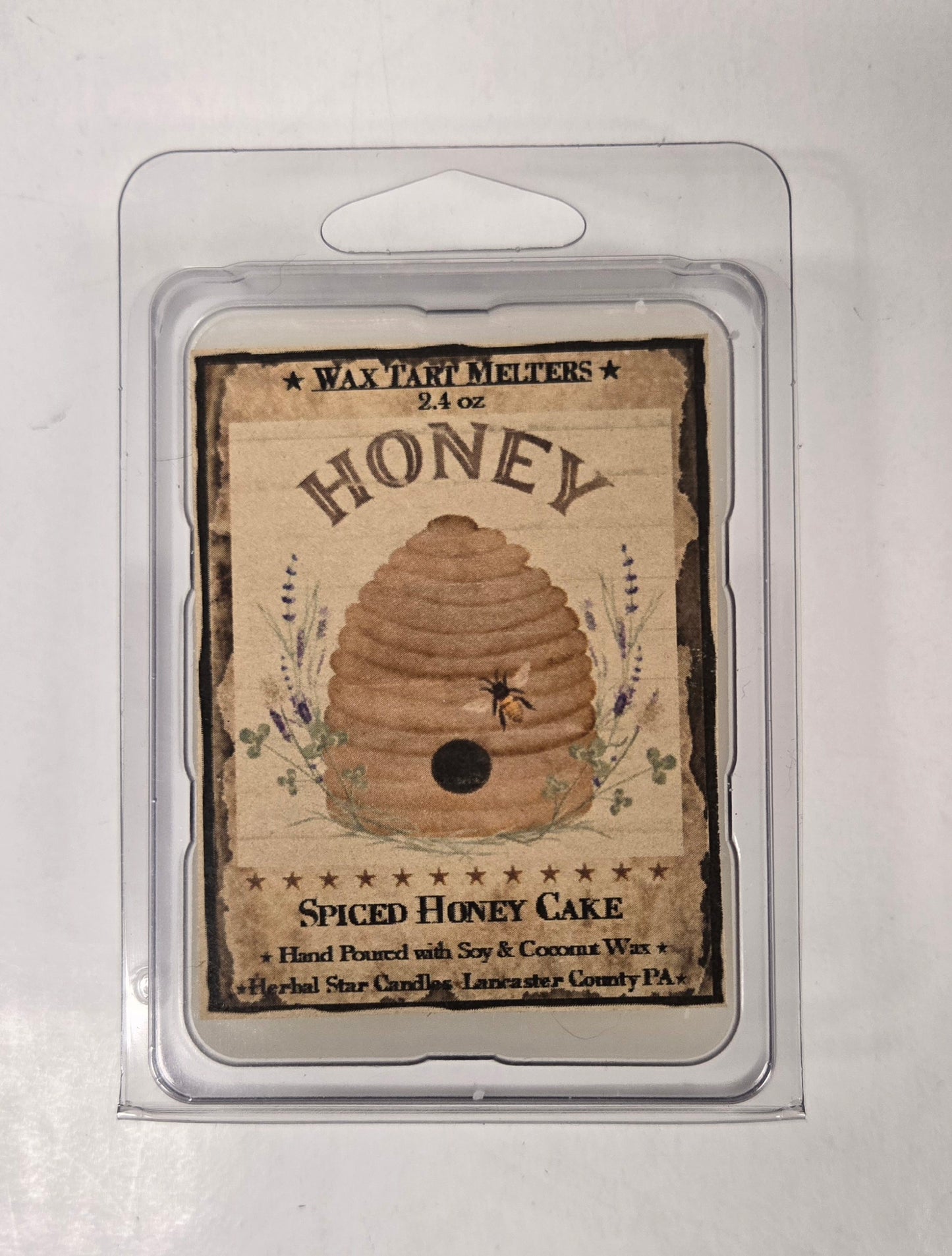 A clear plastic clamshell packaging containing a Spiced Honey Cake mini wax tart with a honeycomb design on the label.
