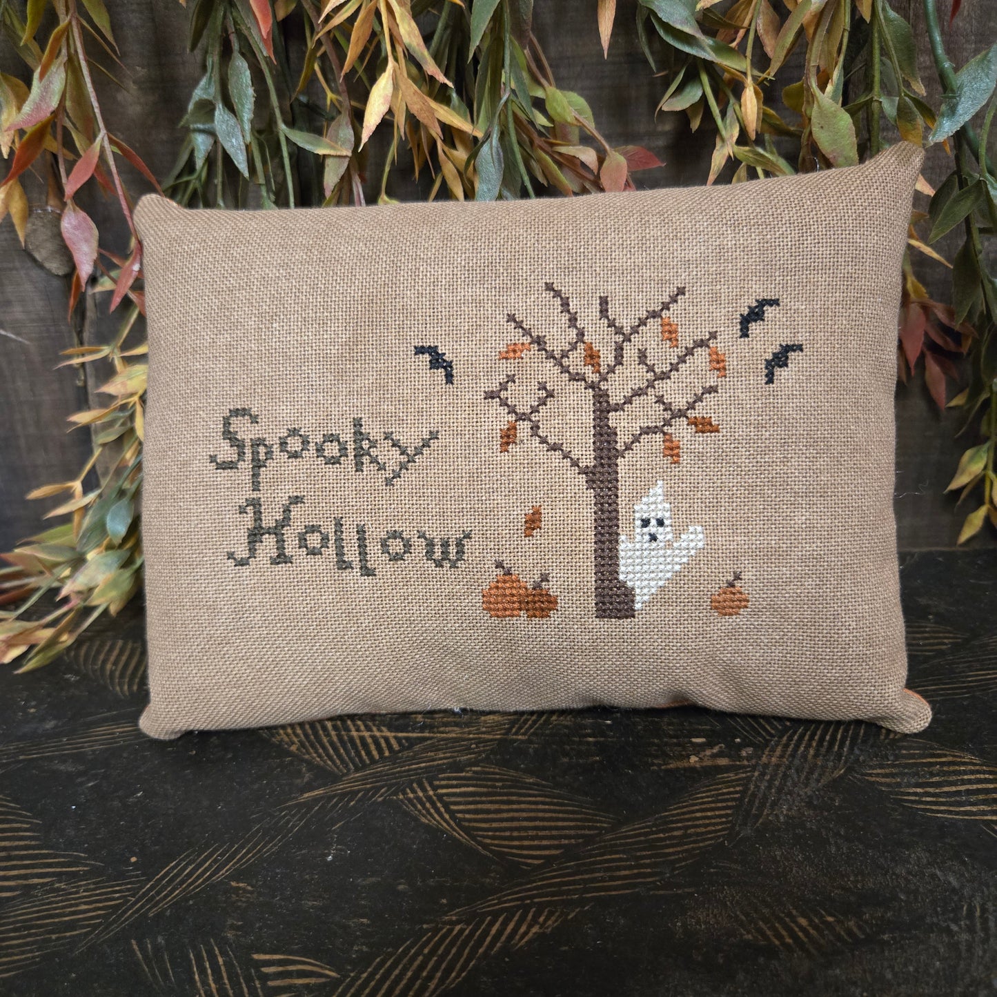 Cross-stitched pillow with ghost design and 'Spooky Hollow' text on a textured surface.