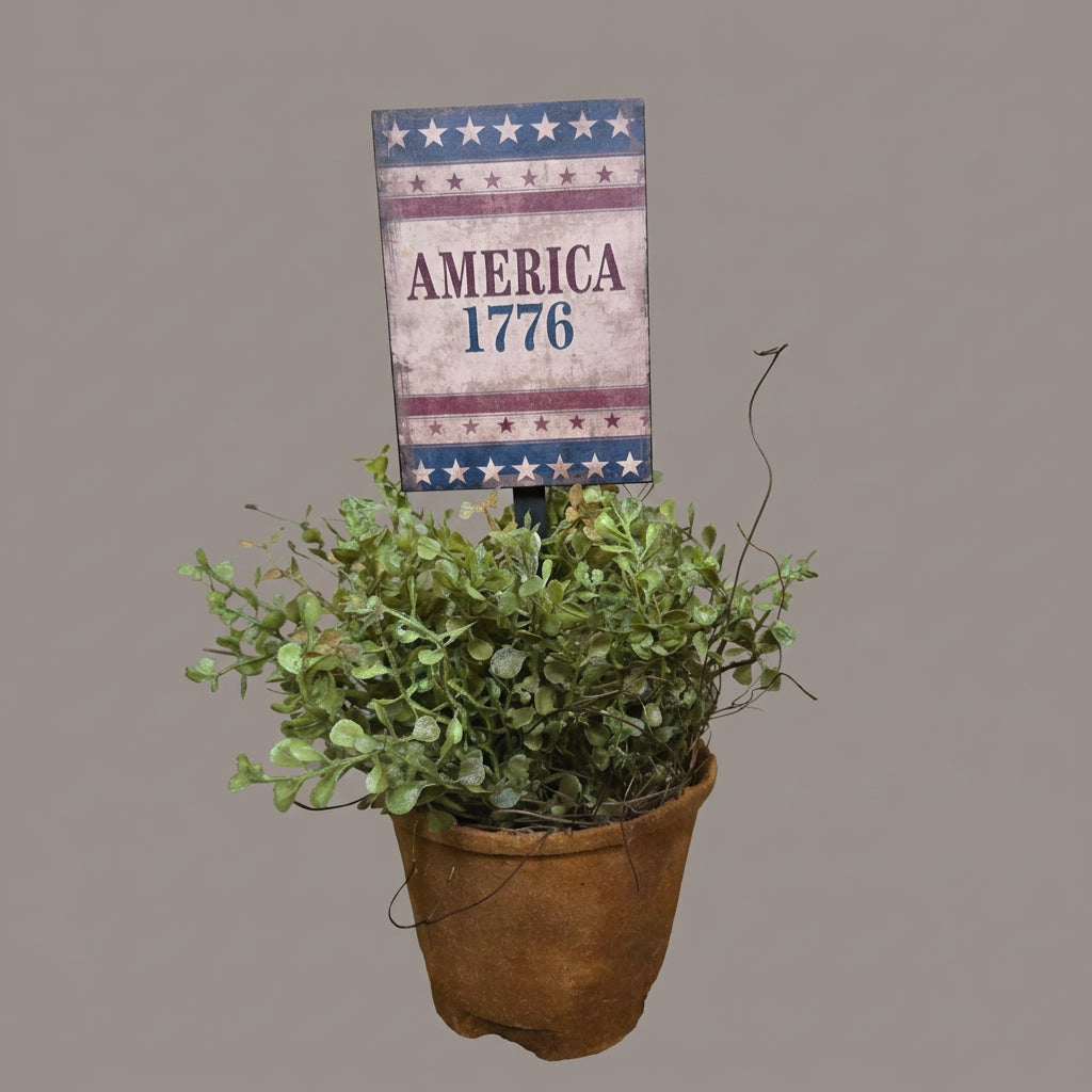Decorative sign with 'America 1776' on a wooden surface with a potted plant.